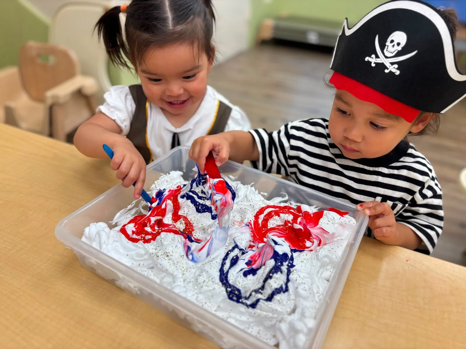 Two children swirling red and blue paint through shaving cream